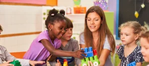 Teacher guiding children in group play, supporting social skill development in children with autism.