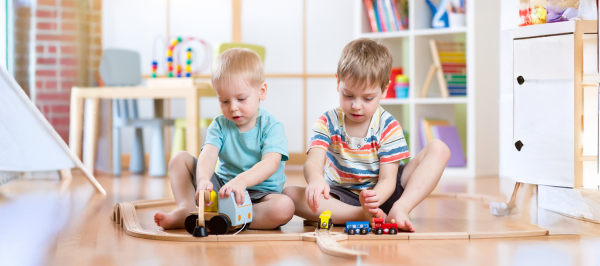 Two young children engage in parallel play in autism by playing side by side with toy trains on separate tracks.
