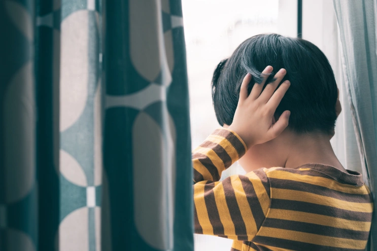 Child covering ears near a window, showing stimming in children with autism and sensory overwhelm.