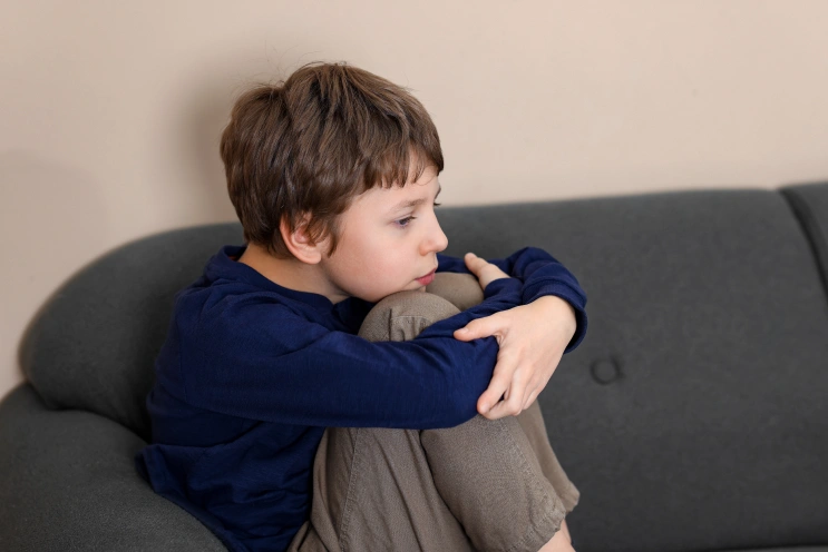 What is sensory overload in autism: child sitting curled up on a couch, hugging knees and looking overwhelmed.